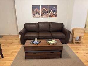 A brown leather sofa, a wooden coffee table with a remote and a book, and a small wooden stool. - Spacious 6-bedroom house in Walhalla, central to all the area attractions (Walhalla)