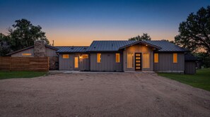 A two-story building with a metal roof, a front entrance with a door, and windows on the second floor. - 3 Acre Luxury  Private Pool + Sports Court (Liberty Hill)