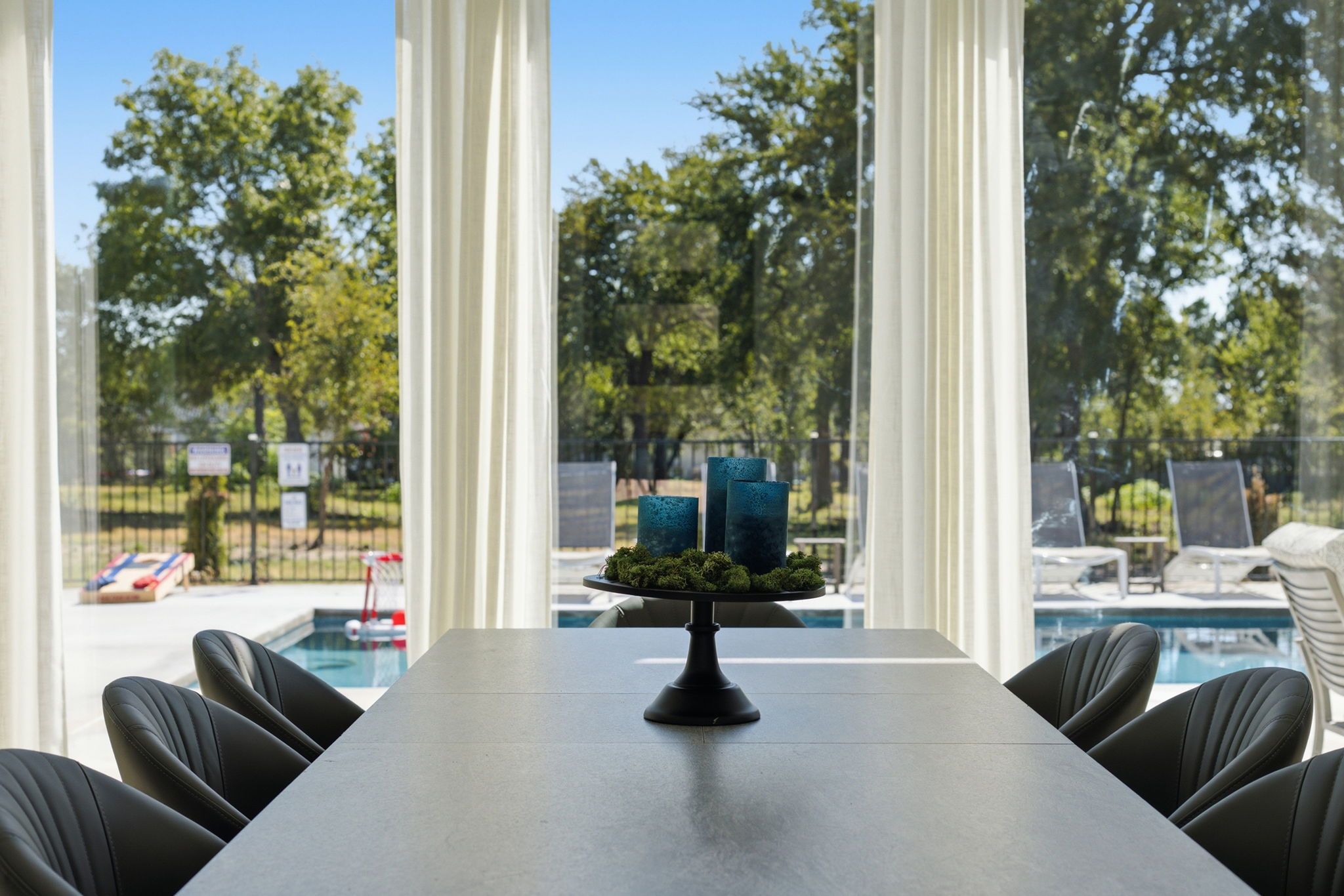 Mesa de conferencias con un centro de mesa decorativo, rodeada de sillas, con vista a una piscina y follaje exterior.
