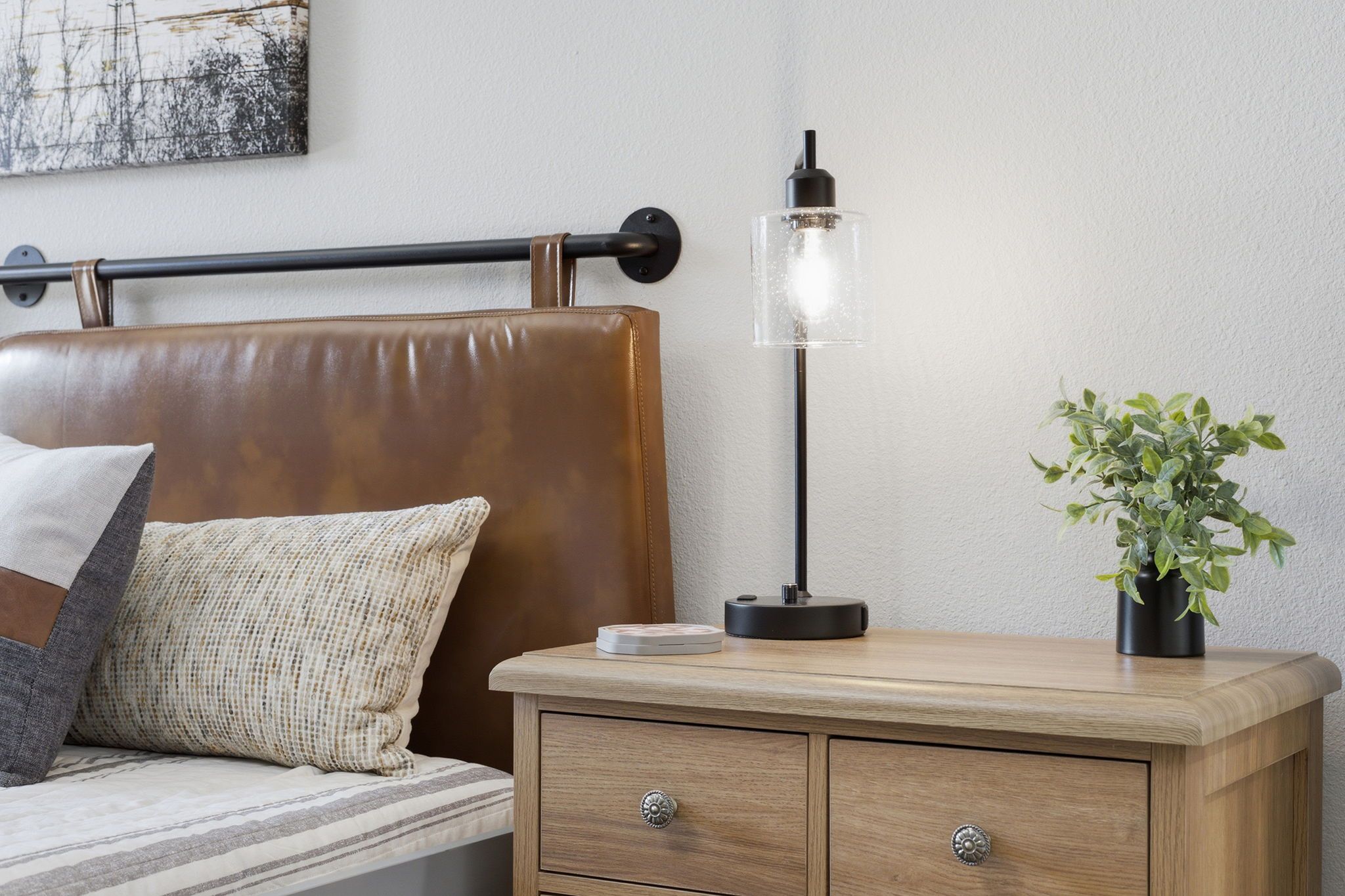 Une chambre à coucher avec un lit, une table de chevet, une lampe et un tableau accroché au mur.