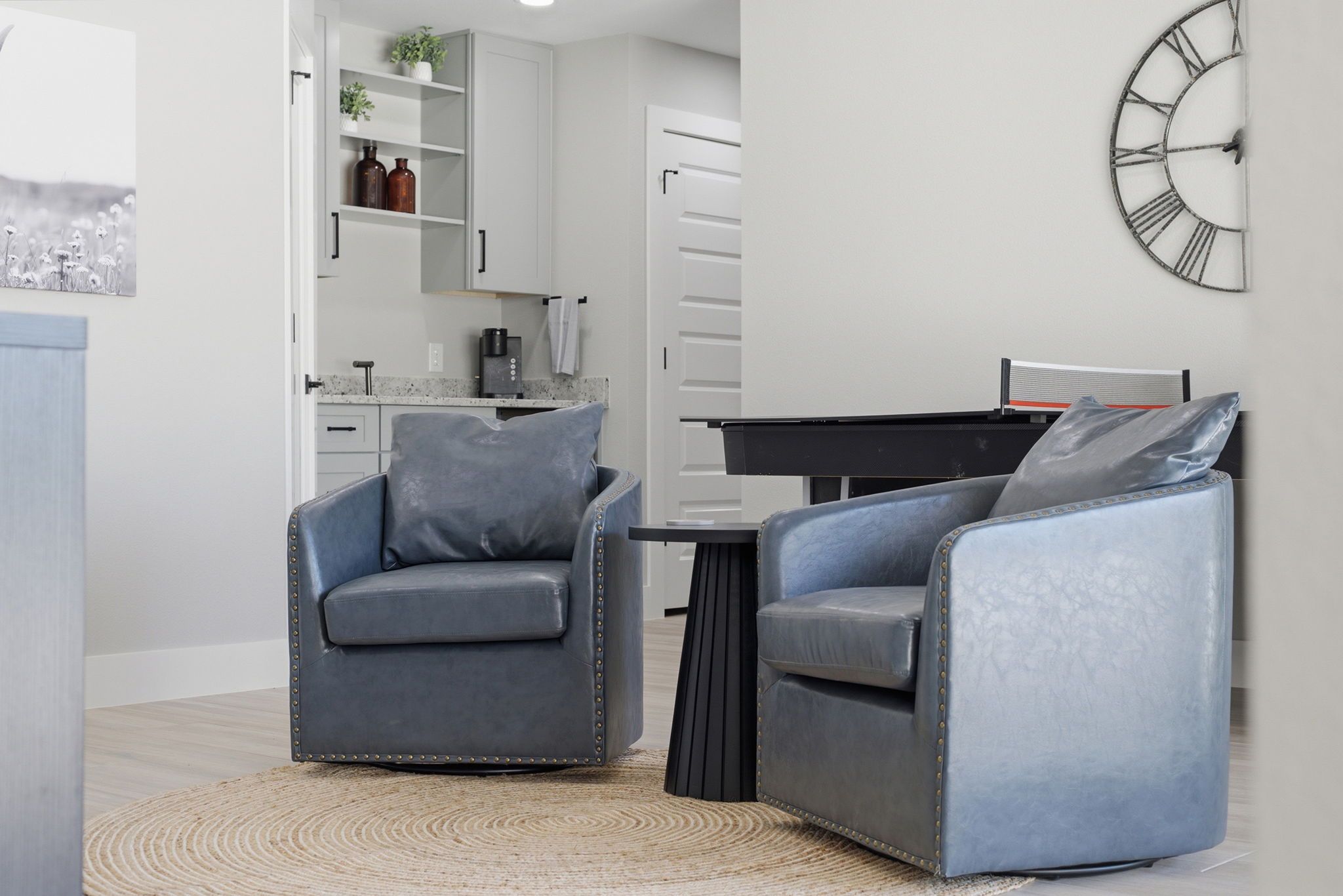 A modern living room with two grey armchairs, a coffee table, and a wall clock.