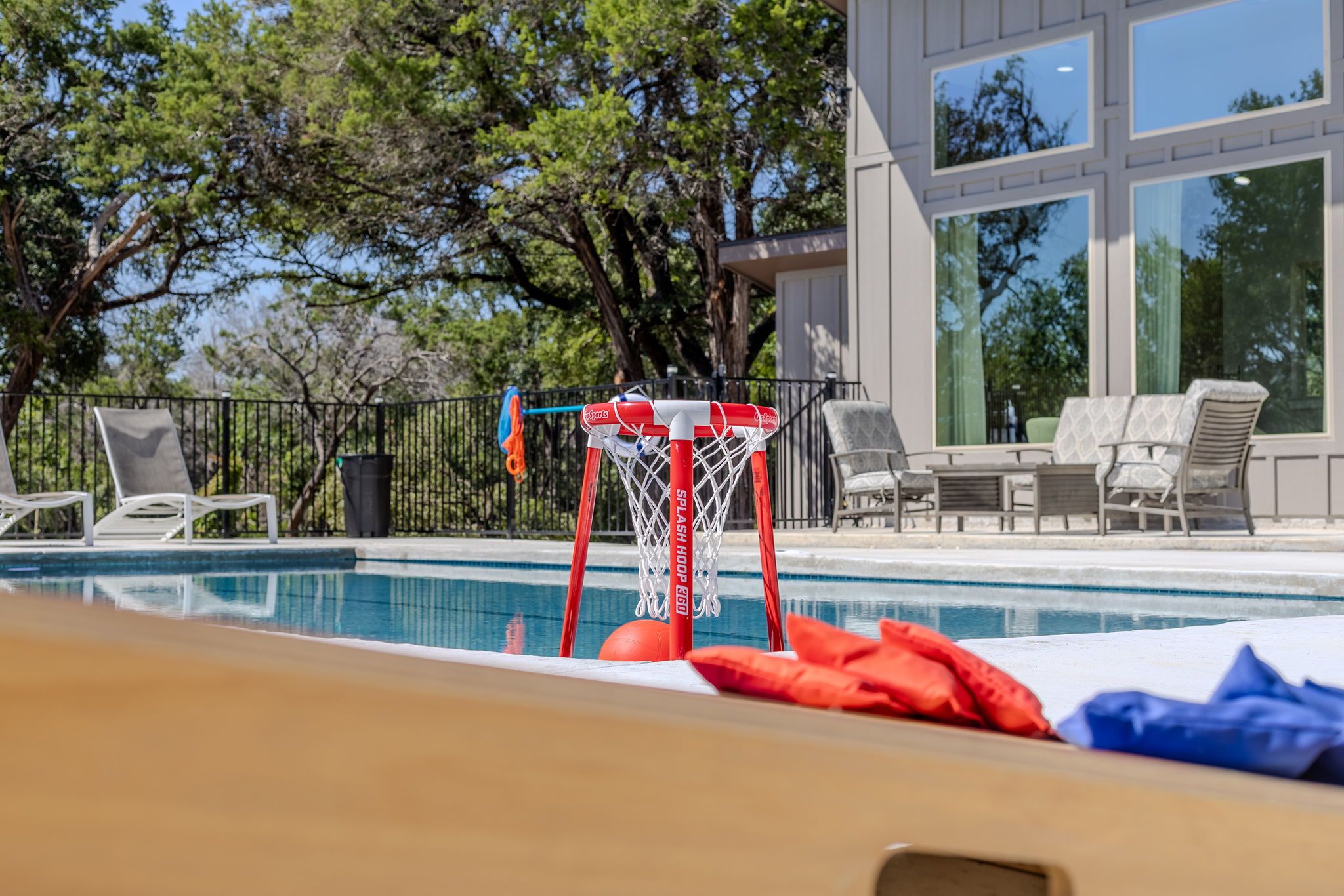A swimming pool with a basketball hoop, lounge chairs, and a building with large windows in the background.