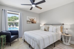 A bedroom with a bed, bedside lamps, a ceiling fan, a window with curtains, and a painting on the wall. - 3 Acre Luxury  Private Pool + Sports Court (Liberty Hill)
