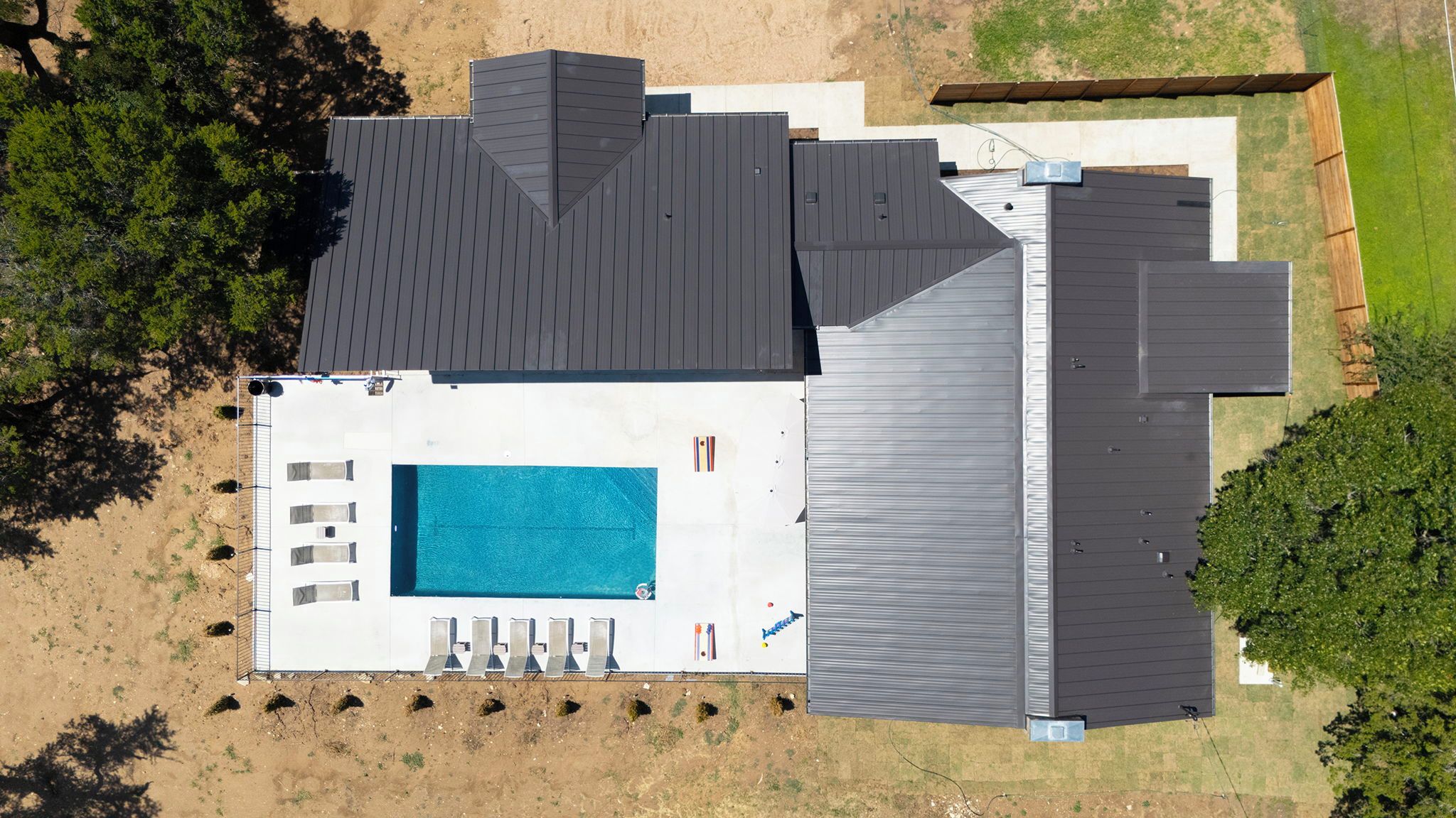 Een modern huis met een groot zwembad, meerdere terrassen en een omheinde achtertuin.