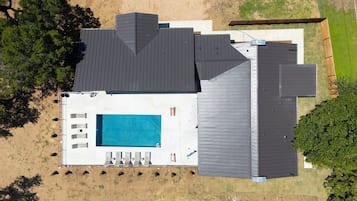 Een modern huis met een groot zwembad, meerdere terrassen en een omheinde achtertuin.