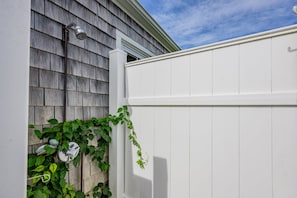 A white exterior wall with a grey shingle roof, a white fence, and green ivy growing along the wall. - Ripple Effect - near the beach and Main Street (Hyannis)