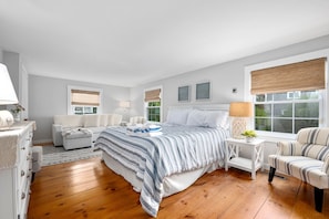 A bedroom with a large bed, two bedside tables, a chair, a dresser, and a window with blinds. - Ripple Effect - near the beach and Main Street (Hyannis)