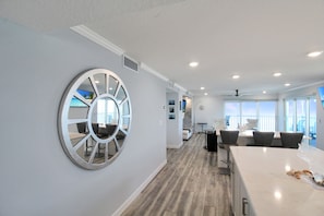 Ein modernes Interieur mit einem großen runden Spiegel, einem Essbereich mit weißem Tisch und Stühlen sowie Blick durch die Fenster.