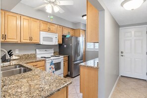 A kitchen with granite countertops, wooden cabinets, a white microwave, a stainless steel refrigerator, and a stove. - Beach Front Condo Venice Shore Bet (Venice)