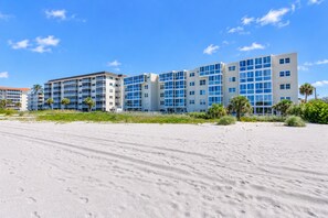 Ein Strandhotel mit mehreren Etagen, großen Fenstern und einem Sandstrand im Vordergrund.