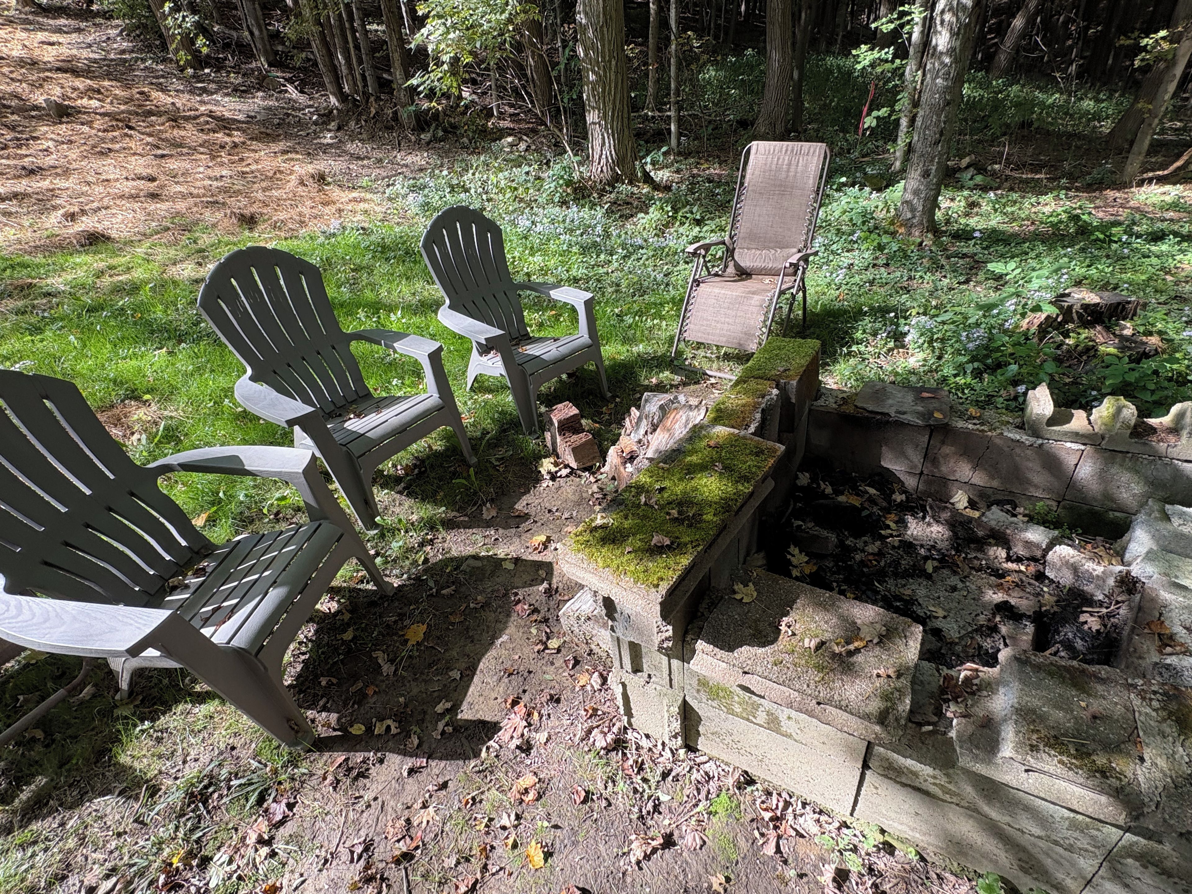 Un campamento con sillas Adirondack y un brasero rodeado por un muro de piedra.