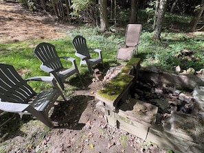 Un campamento con sillas Adirondack y un brasero rodeado por un muro de piedra.