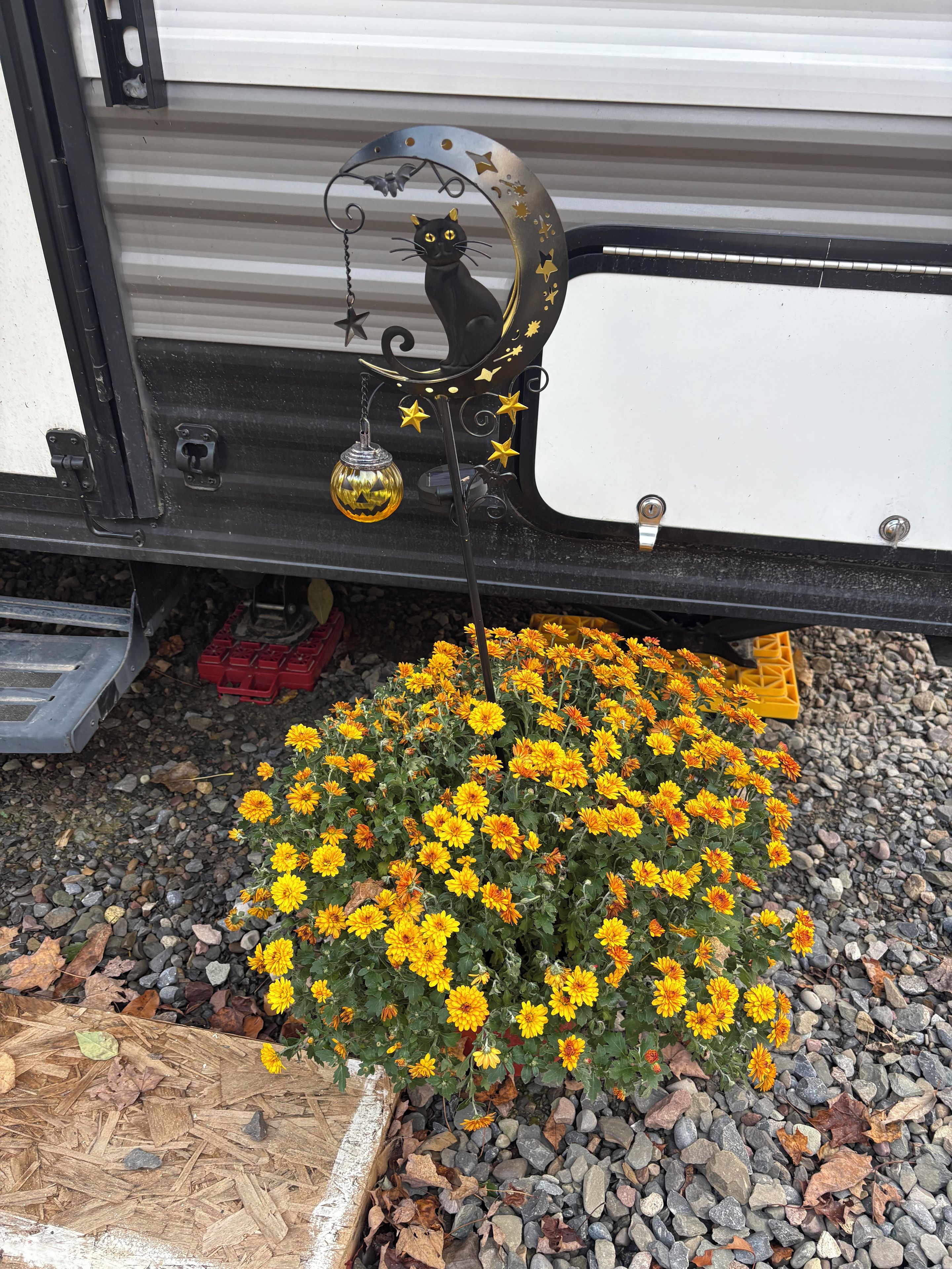 A decorative metal cat sculpture with a hanging ornament and stars, positioned under a vehicle.