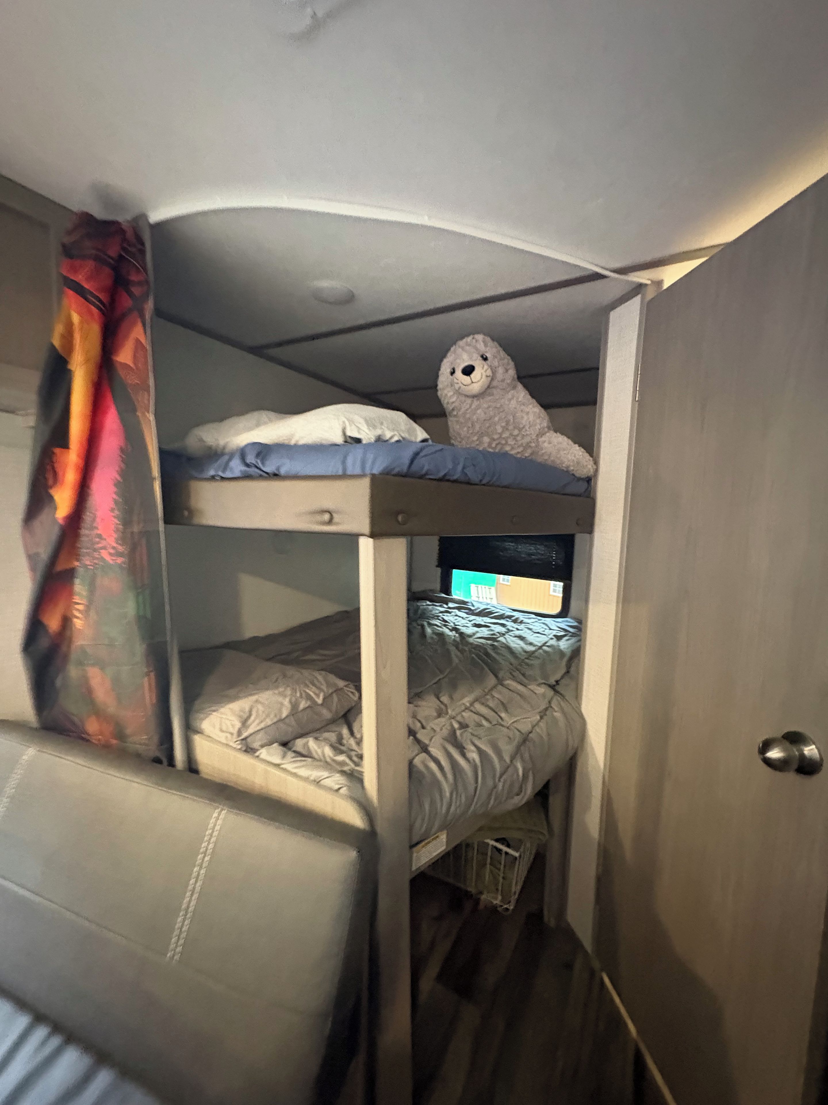 Una cama litera con un oso de peluche en la parte superior, una silla y una puerta.