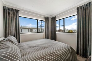 Ein Hotelzimmer mit einem großen Bett, zwei Fenstern und Blick auf ein Gebäude.