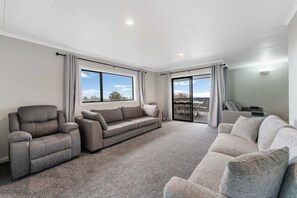 A spacious living room with a large sofa, a recliner, and a view through a sliding glass door to an outdoor patio. - Taupō Group Getaway | 6 Bedrooms, 3 Bathrooms (Taupō)