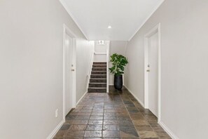 A hallway with a staircase, white walls, and a potted plant. - Taupō Group Getaway | 6 Bedrooms, 3 Bathrooms (Taupō)