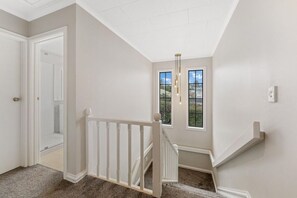 A hallway with a white railing, a door, and a window with a view of greenery. - Taupō Group Getaway | 6 Bedrooms, 3 Bathrooms (Taupō)