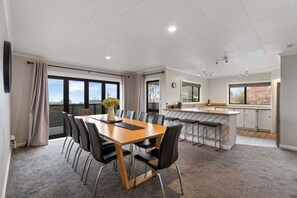 A modern kitchen with a bar area, a dining table with chairs, and large windows providing natural light. - Taupō Group Getaway | 6 Bedrooms, 3 Bathrooms (Taupō)