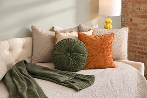 A bed with a quilted headboard, multiple pillows, and a green throw blanket. - The Bentley Collection - The Retro Retreat (Dallas)