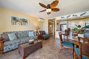 A living room with a sofa, coffee table, and chairs, a dining area with a table and chairs, a kitchen with cabinets and appliances, and a ceiling fan. - Oceanfront Ground-Floor Condo, Papakea Maui (Lahaina)
