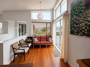 Un salon moderne avec un canapé, des fauteuils, une table et une grande fenêtre équipée de stores.