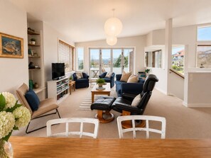 A spacious living room with a large window, a television, and a variety of seating options. - Modern Family Bach | Walk to the Lake | Sleeps 8 (Taupō)