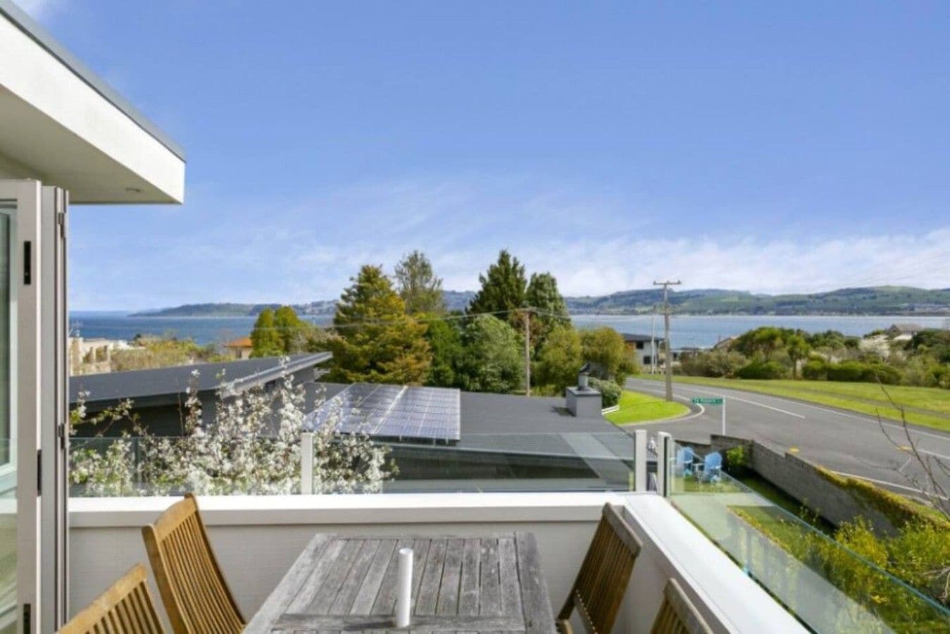 A balcony with a view of a body of water, a road, and a hilly landscape.