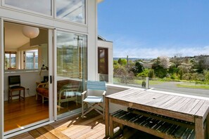 A modern house with a balcony, a dining table, and a view of the landscape. - Modern Family Bach | Walk to the Lake | Sleeps 8 (Taupō)