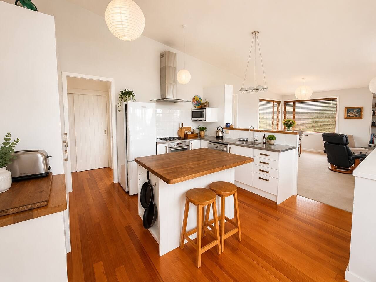 A modern kitchen with a central island, wooden flooring, white cabinetry, and a dining area with a chair.