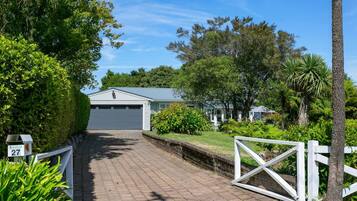 A residential property with a paved driveway leading to a garage, surrounded by lush greenery and a white fence.