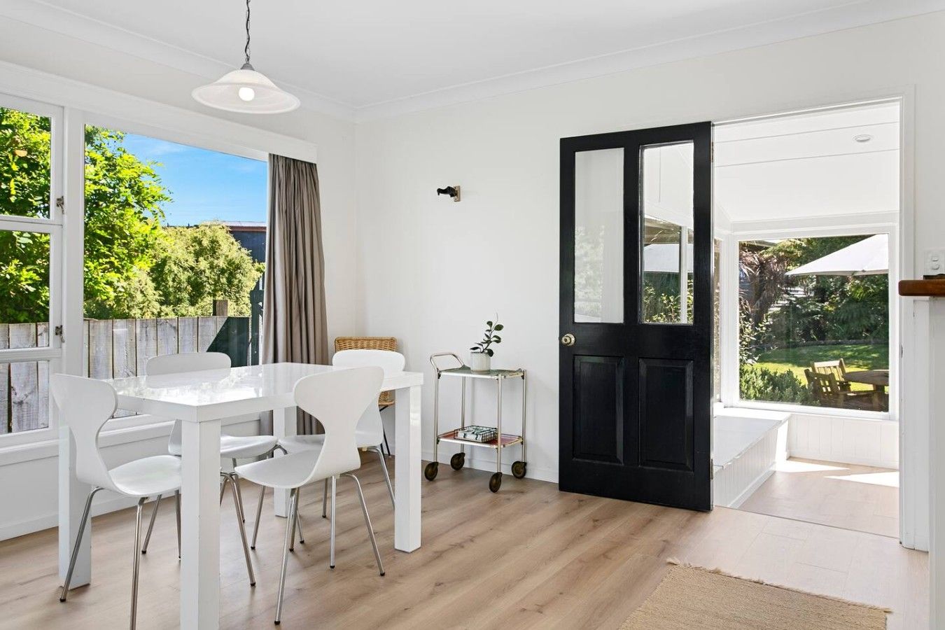A bright room with a dining table and chairs, a black door, and large windows.