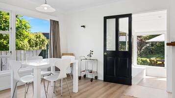 A bright room with a dining table and chairs, a black door, and large windows.