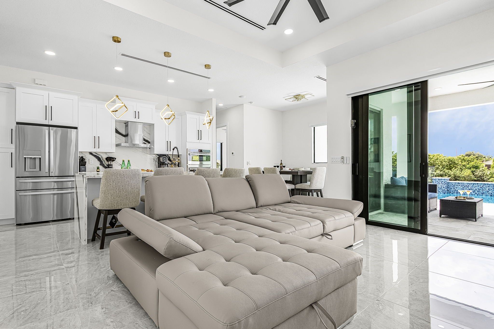 A modern living room with a sectional sofa, a kitchen with white cabinets, and a dining area.