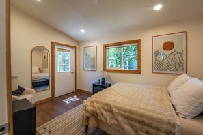 Ein Schlafzimmer mit einem Bett, einem Nachttisch, einer Lampe, einem Spiegel und Kunstwerken an den Wänden.