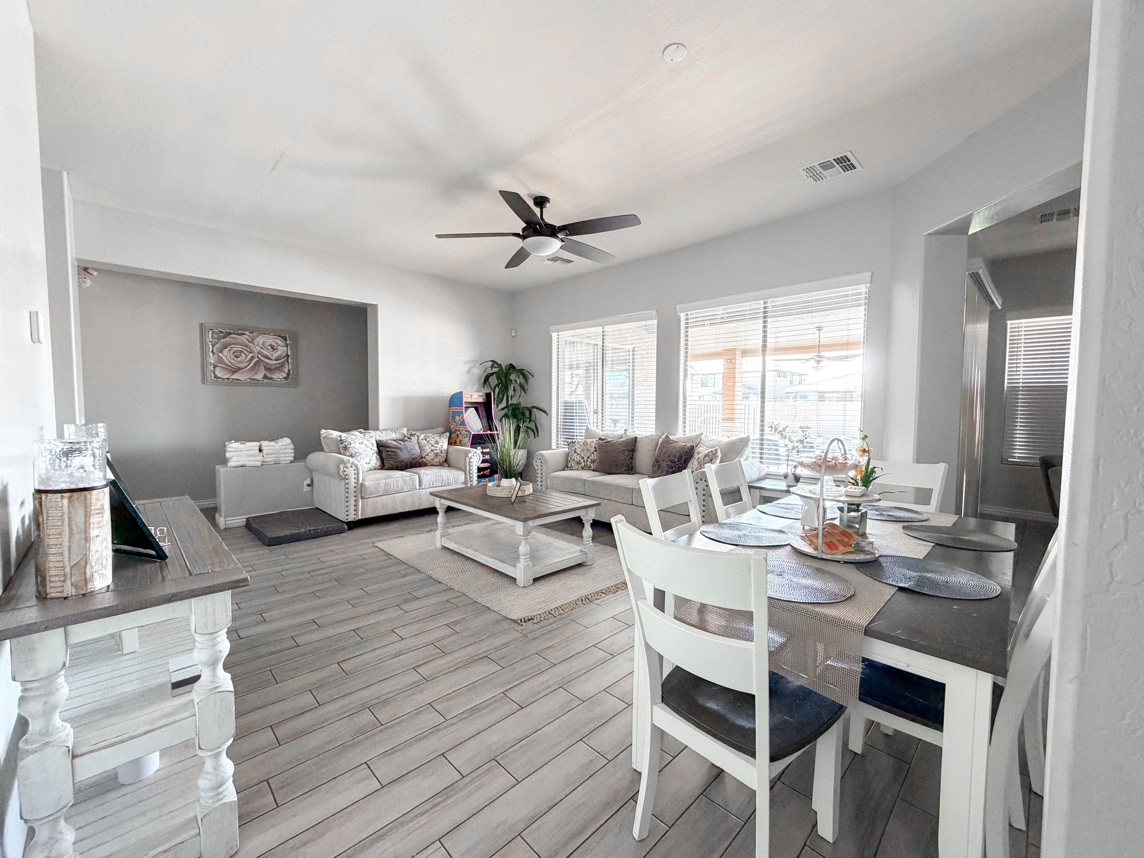 A spacious living area with a dining table, white furniture, and a ceiling fan.