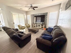 A living room with two sofas, a coffee table, and a TV against a stone wall. - Lovely 4-bedroom house with pool in charming Avondale (Avondale)
