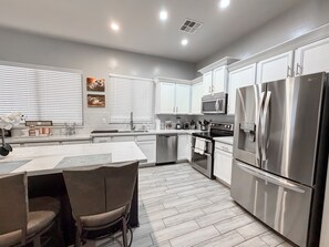 A modern kitchen with white cabinetry, stainless steel appliances, and a central island with seating. - Lovely 4-bedroom house with pool in charming Avondale (Avondale)