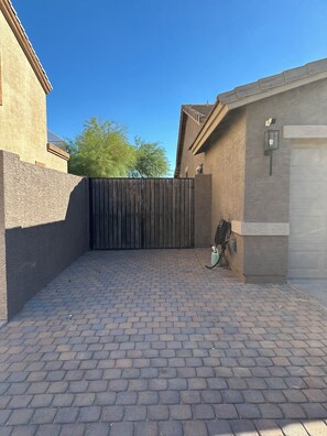 A paved driveway leading to a gated entrance with a metal fence, a garage door, and a wall-mounted light fixture. - Lovely 4-bedroom house with pool in charming Avondale (Avondale)