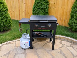 Un barbecue portable NEXGRILL Daytona, doté d’une table d’appoint, d’une bouteille de gaz et d’ustensiles de cuisson.