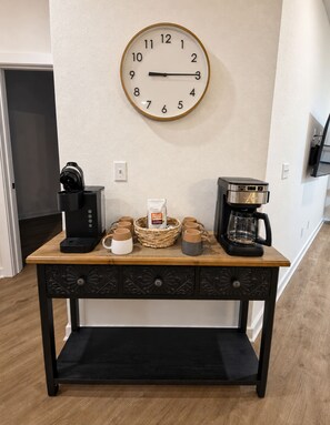 Un coin café avec deux machines à café, une horloge et un panier rempli de tasses à café, le tout posé sur une table en bois.
