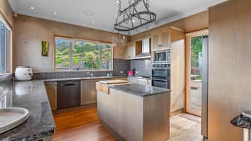 A modern kitchen with a central island, stainless steel appliances, and a view of a garden through large windows.