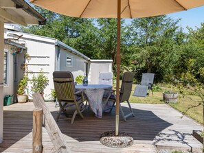 Eine Terrasse im Freien mit Tisch und Stühlen, umgeben von einer Holzterrasse und einem überdachten Bereich mit Sonnenschirm.