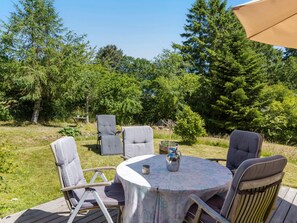 Eine Terrasse im Freien mit einem runden Tisch und vier Stühlen, umgeben von einer Holzterrasse und einem Baumhintergrund.