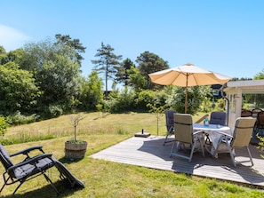 Ein Außenbereich mit einer Holzterrasse, einem Tisch mit Stühlen und einem großen Sonnenschirm.