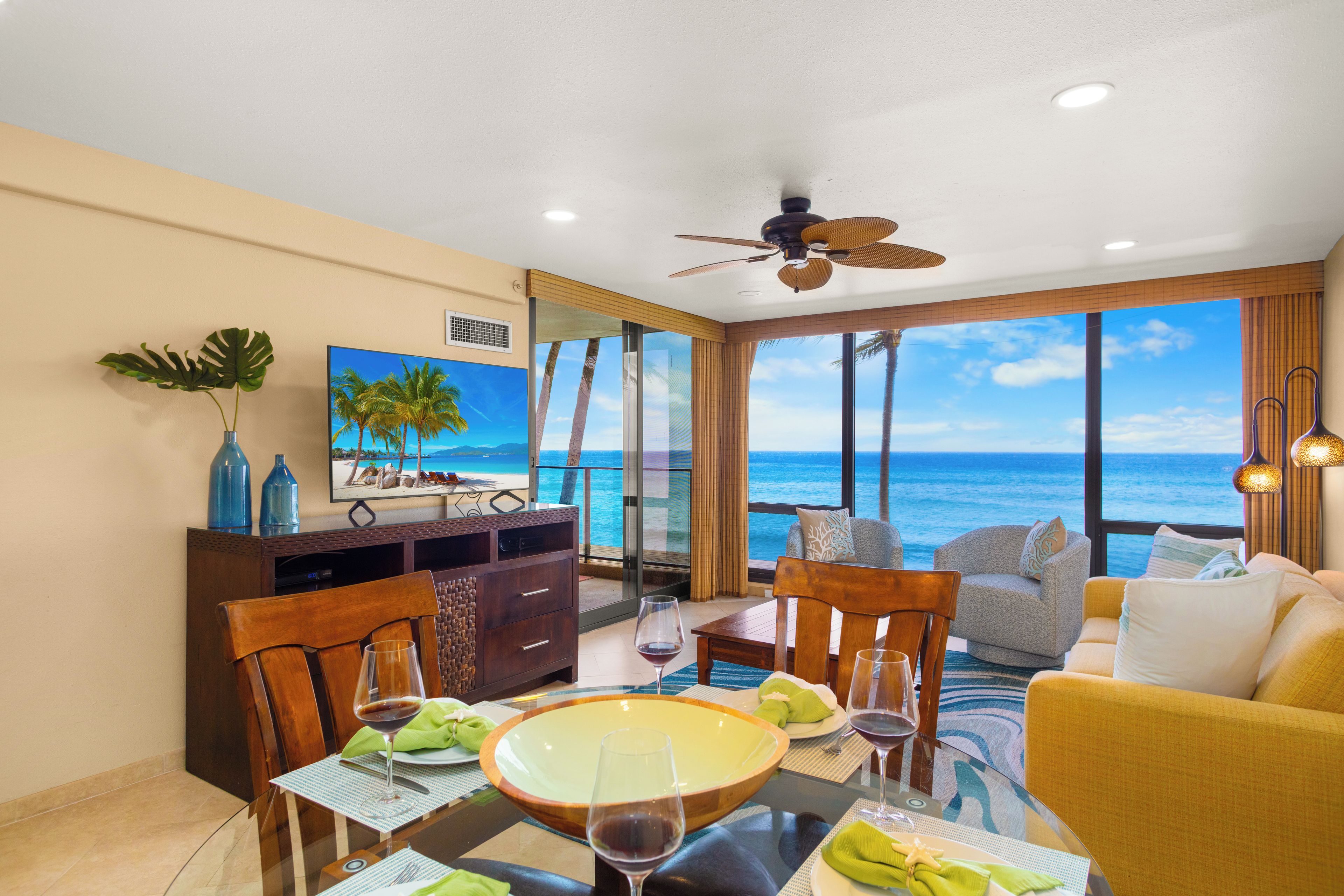 A room with a dining table, chairs, a sofa, and a view of the ocean.