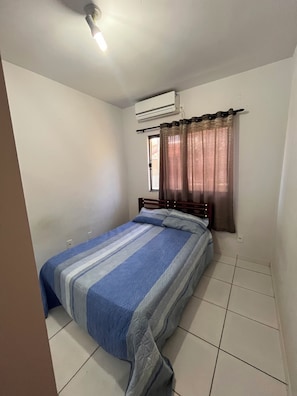 A room with a bed, an air conditioning unit, a window with curtains, and a ceiling light. - House in a Gated Community - Caldas Novas, Goiás (Caldas Novas)