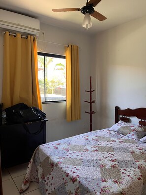 A bedroom with a bed, a window with curtains, a ceiling fan, and an air conditioning unit.