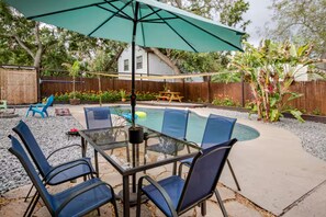 Ein Garten mit einem Glastisch, Stühlen, einem Pool und einem Sonnenschirm auf der Terrasse.