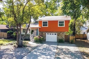 A two-story house with a garage, surrounded by trees and a gravel driveway. - Private Pool Oasis | 3BR Home Near Busch Gardens (Tampa)